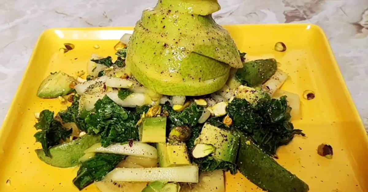 A green salad with avocado, pear, cucumber, and kale on a yellow square plate.